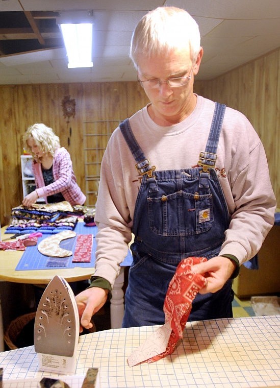 Jon Whitmore irons one of the familys moist-heat therapeutic packs in preparation for a sale this weekend. In the background his daughter, Lisa, 13, wraps and stacks items for the sale.