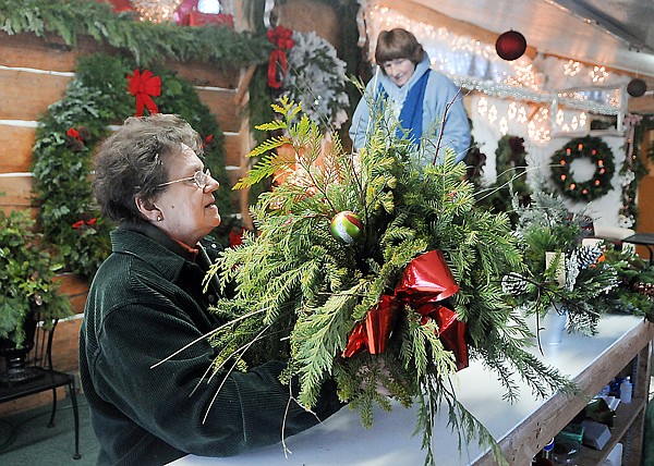 Gloria Henderson, left, and Terry Eaker hanging baskets of mixed Christmas green on Friday at the Snow Line Tree Company.