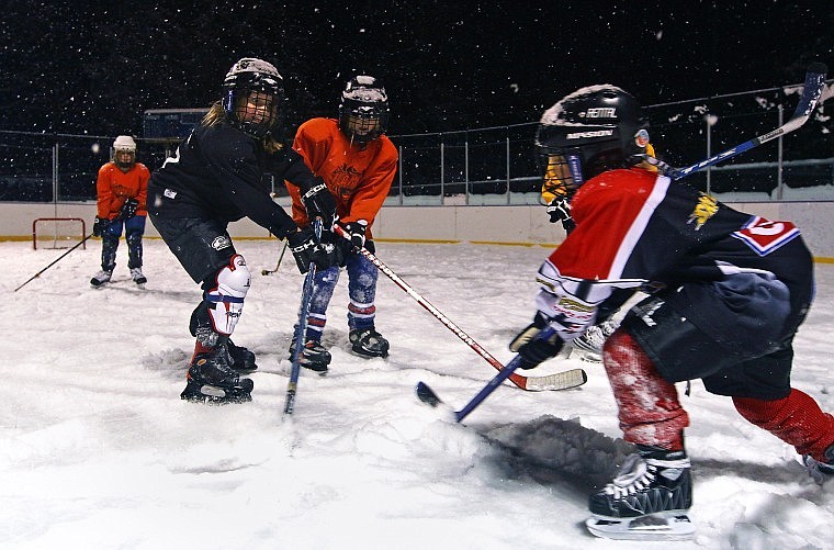 Shae Anderson shoots the puck hidden in the snow while Jascah Vann defends the goal Tuesday evening at the Woodland Park Ice Rink Tuesday evening. Girls aged 5-11 were invited to play and recieve some help from the U-19 Girls Hockey team.