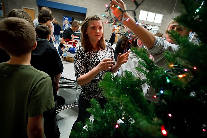 &lt;p&gt;JEROME A. POLLOS/Press Shannon Kempton steps out of the way of Jacob Koski as he strings lights on one of three Christmas trees being decorated Tuesday for families in need. Junior Honor Society students from River City Middle School decorated trees and assembled gift baskets with toys, holiday decorations, food and gift cards for families of students who attend their school. Post Falls Middle School will also be assembling gift baskets for needy families Wednesday with the second half of the $700 in fund raised for the project between the two schools.&lt;/p&gt;