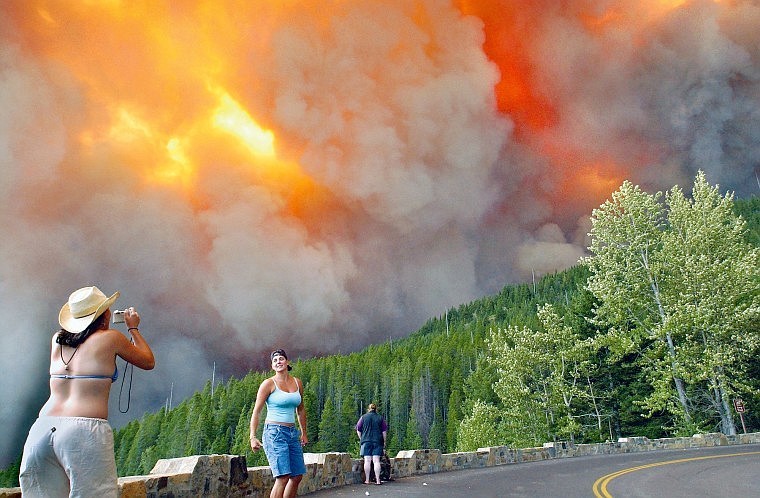 As the Trapper Creek Fire in Glacier National Park comes dangerously close to the Loop on July 23, 2003, Kim Barger, left, and Katie Weaver of Missoula take pictures of each other posing in front of the approaching fire. Shortly after the photo was taken, the women and others at the Loop were told to leave by park rangers and Going-to-the-Sun Road was closed. For more on the fires of 2003, go to Page A4.