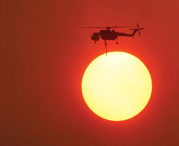 As the setting sun is colored by smoke from the Robert Fire on July 29, 2003, a firefighting helicopter battles fires burning in Glacier National Park. The fire caused the evacuation of hundreds of homes and shut down a large section of Glacier National Park for a time during the summer of 2003.