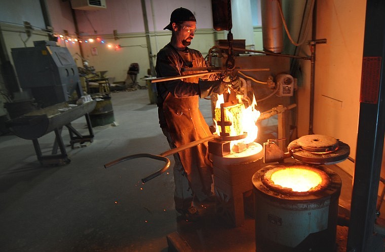 Coby Johnson removes a crucible of molten bronze from the oven as he prepares to pour four sculptures on Thursday in Kalispell.