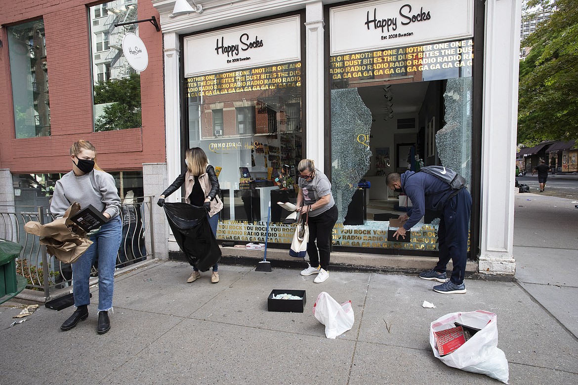 Neighbourhood volunteers clean up broken glass at a Happy Socks store in the SoHo neighbourhood of New York, Monday, June 1, 2020. Protesters broke into the store Sunday night in reaction to George Floyd's death while in police custody on May 25 in Minneapolis. (AP Photo/Mark Lennihan)