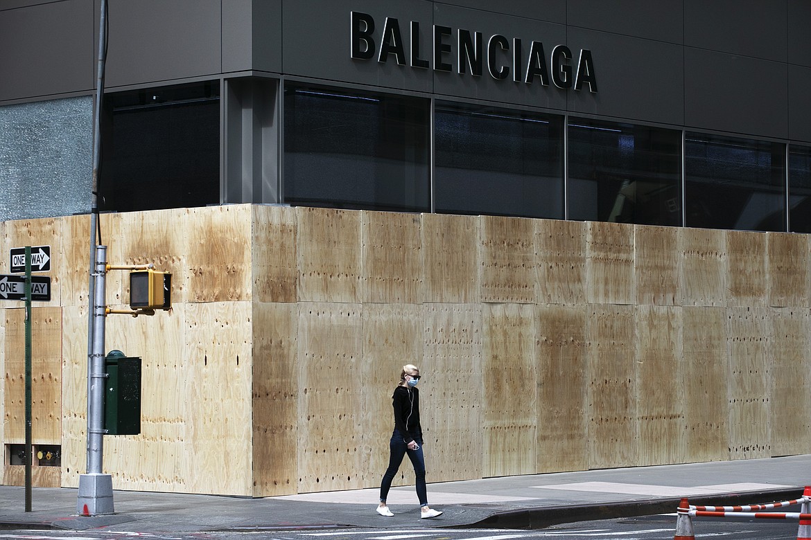 A woman walks by a boarded up Balenciaga store, Tuesday, June 2, 2020, on Madison Avenue in New York. Protesters broke the window Monday night in reaction to the death of George Floyd, a black man who died after being restrained by Minneapolis police officers on May 25, (AP Photo/Mark Lennihan)