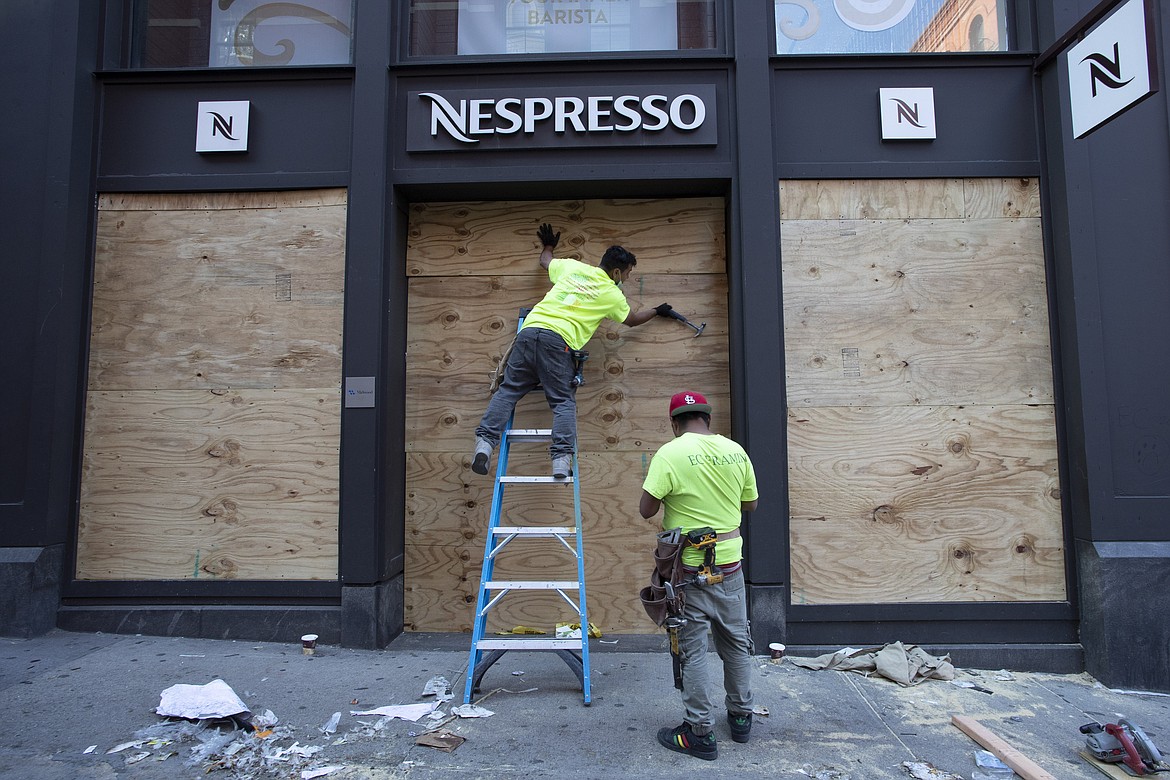Workers board up windows of a Nespresso store, Monday, June 1, 2020, in the SoHo neighbourhood of New York. Protesters broke into the store Sunday night in reaction to George Floyd's death while in police custody on May 25 in Minneapolis. (AP Photo/Mark Lennihan)