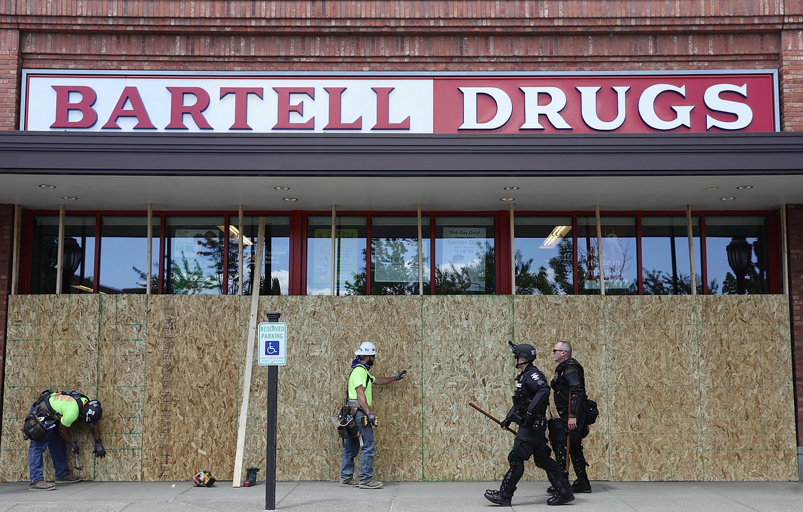 Businesses are boarded up as police walk past at University Village mall Monday, June 1, 2020, in Seattle, in the wake of national protests sparked by the death of George Floyd in Minneapolis. The mall is completely shut down with a police line restricting access at the south entrance. (Ken Lambert/The Seattle Times via AP)
