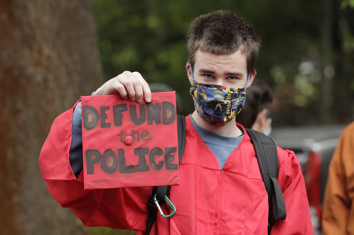 Elliot Armitage, a 2020 graduate of Ballard High School, holds his mortarboard cap that reads "Defund the Police" as he prepares to take part in a cap and gown Black Lives Matter march with other high school graduates, Monday, June 15, 2020, in Seattle. The theme of the march as "Walking for Those Who Can't," and organizers were calling for police funding reforms and an end to Seattle public schools' relationship with the Seattle Police Department. (AP Photo/Ted S. Warren)