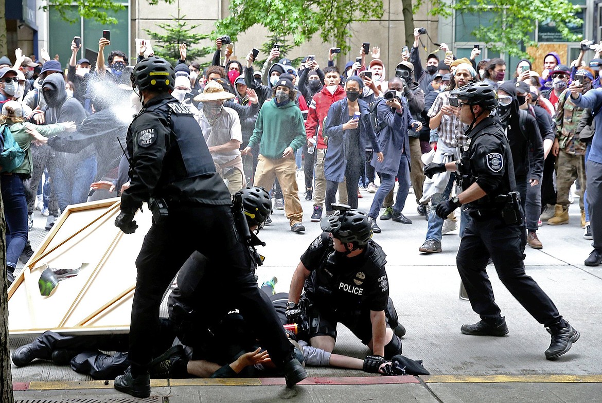 Protesters surrounding police officers making an arrest are pepper sprayed in downtown Seattle, Sunday, May 31, 2020, as demonstrations continue over the death of George Floyd. Floyd died after being restrained by Minneapolis police officers on May 25. (Ken Lambert/The Seattle Times via AP)