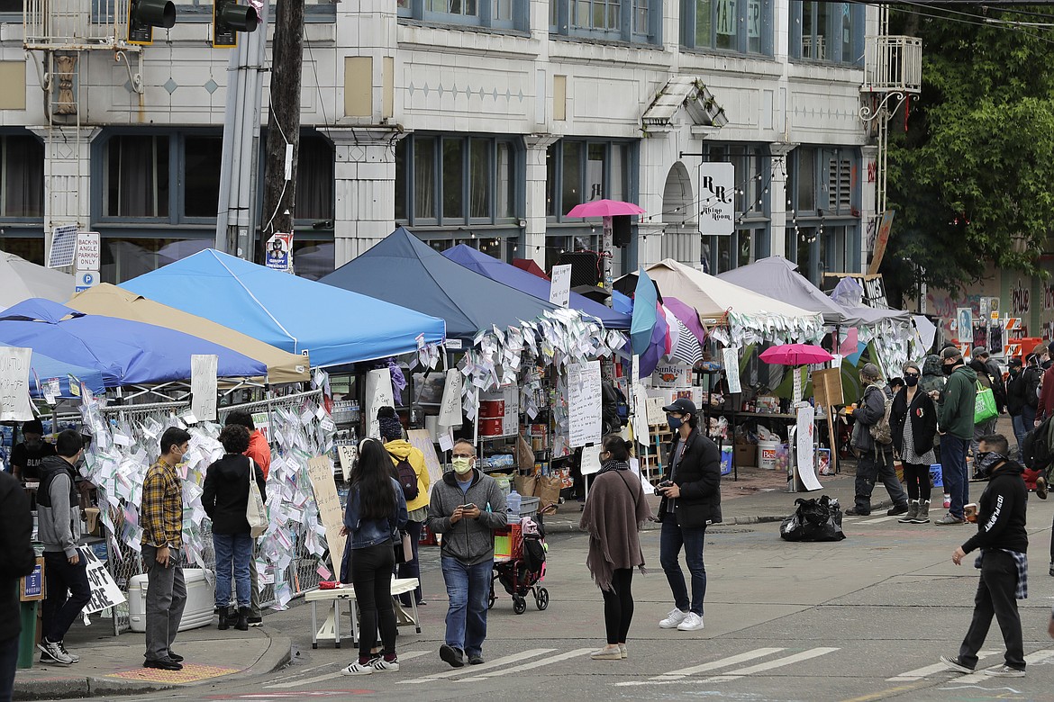 People walk near tents that make up the "No Cop Co-op," Monday, June 15, 2020, inside what has been named the Capitol Hill Occupied Protest zone in Seattle. Protesters have taken over several blocks near downtown Seattle after officers withdrew from a police station in the area following violent confrontations. (AP Photo/Ted S. Warren)