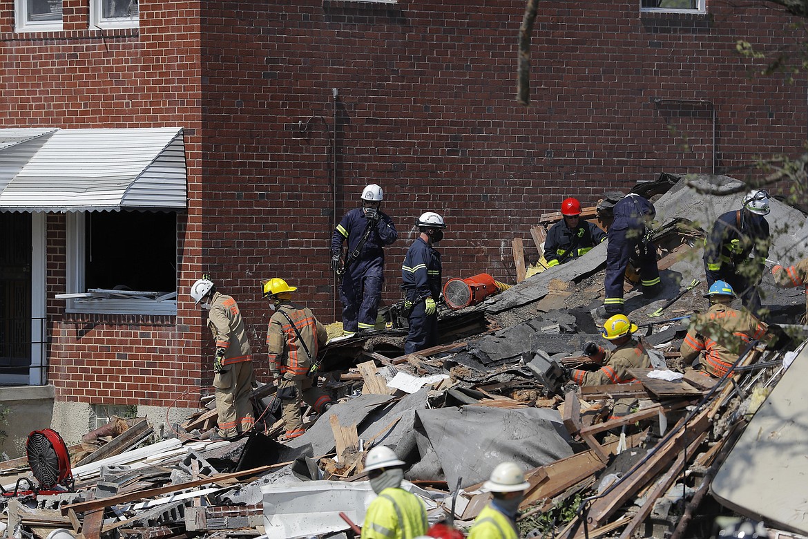 Authorities walk among the piles of debris from an explosion in Baltimore on Monday, Aug. 10, 2020. The "major gas explosion" that involved three houses at Labyrinth and Reistertown roads has left multiple people, including children, trapped according to the Baltimore Fire Department. (AP Photo/Julio Cortez)
