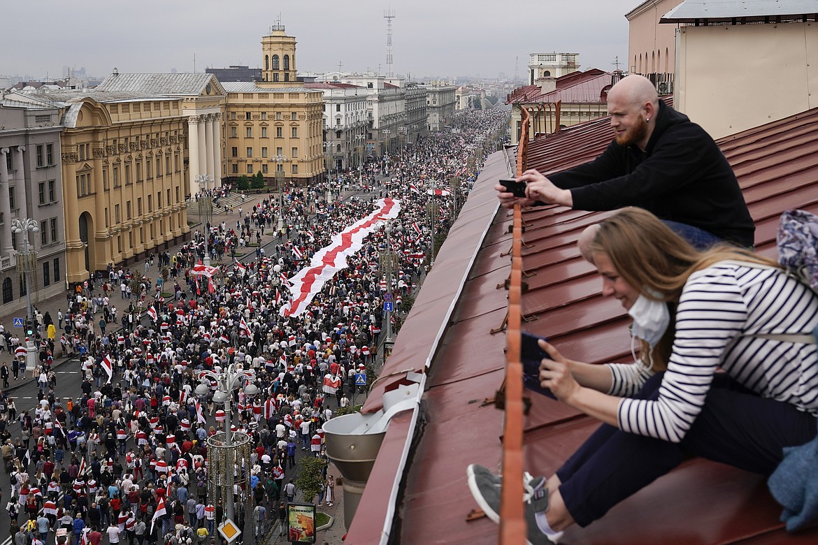 People take photos sitting on the roof as Belarusian opposition supporters with a huge old Belarusian national flag march to Independence Square in Minsk, Belarus, Sunday, Aug. 23, 2020.  A vast demonstration with many thousands of protesters demanding the resignation of Belarus' authoritarian president are rallying in the capital, continuing the public dissent since the disputed presidential election. (AP Photo/Evgeniy Maloletka)