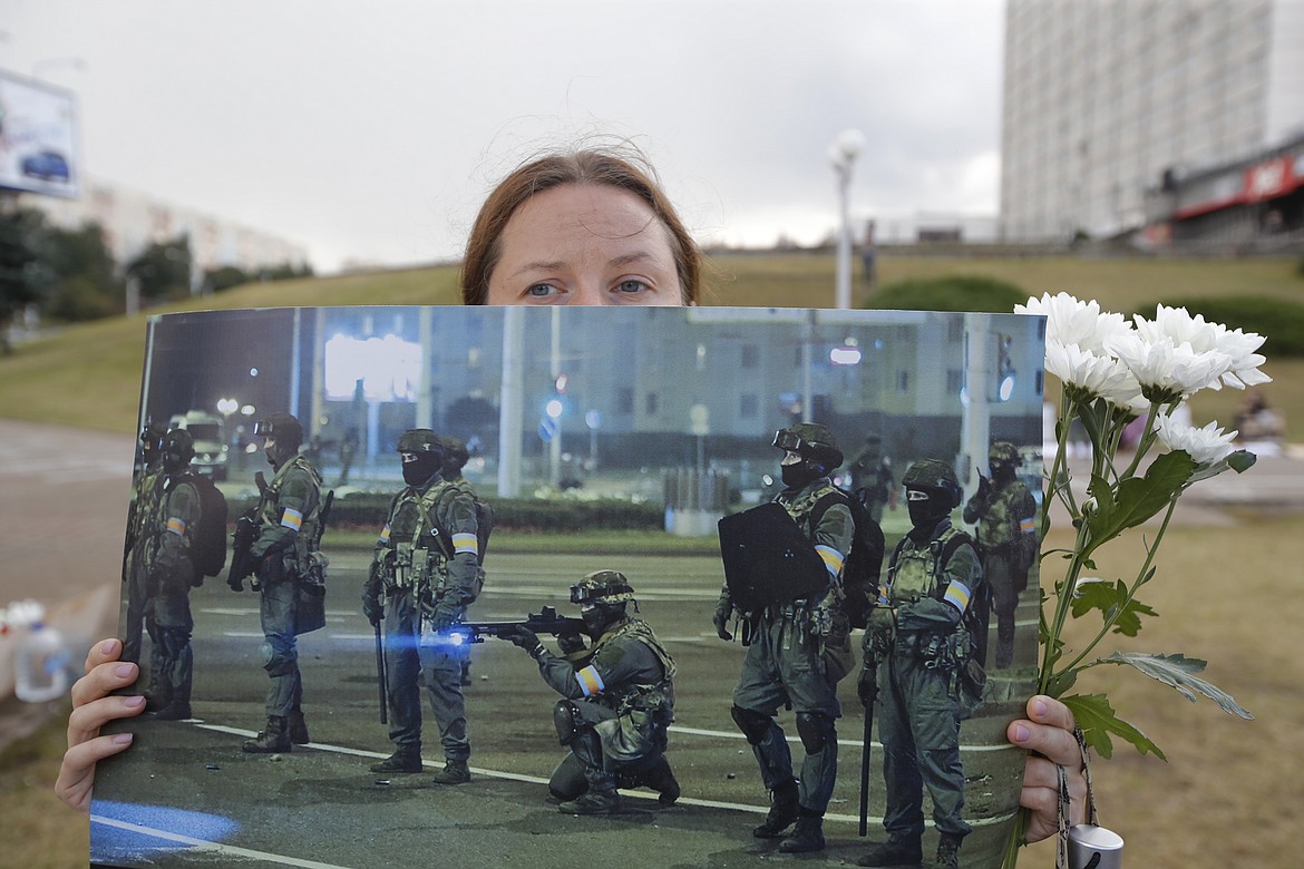 A woman holds a picture of Belarusian police as people stand near the place where Alexander Taraikovsky died amid the clashes protesting the election results, in Minsk, Belarus, Monday, Aug. 24, 2020. Belarusian authorities on Monday detained two leading opposition activists who have helped spearhead a wave of protests demanding the resignation of the country's authoritarian ruler of 26 years. (AP Photo/Dmitri Lovetsky)