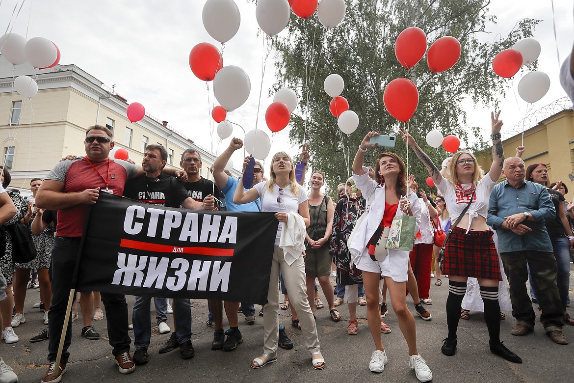 People with a banner reading "Country for life" prepare to release balloons in colors of old Belarusian national flag into the sky to show their solidarity with the detainees at a detention centre during opposition rally in Minsk, Belarus, Tuesday, Aug. 18, 2020. After the police crackdown at least 7,000 were detained by riot police, with many complaining they were beaten mercilessly. (AP Photo/Sergei Grits)