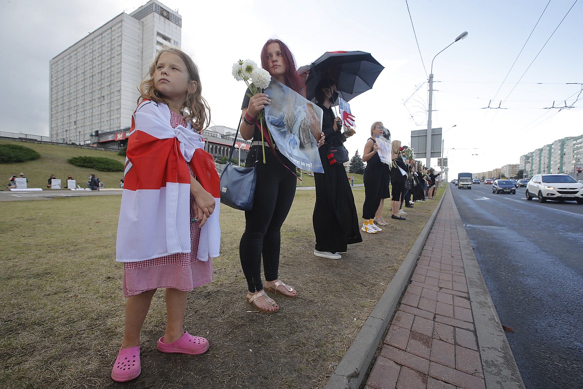 A girl covers with an old Belarusian National flag as people stand near the place where Alexander Taraikovsky died amid the clashes protesting the election results, in Minsk, Belarus, Monday, Aug. 24, 2020. Belarusian authorities on Monday detained two leading opposition activists who have helped spearhead a wave of protests demanding the resignation of the country's authoritarian ruler of 26 years. (AP Photo/Dmitri Lovetsky)