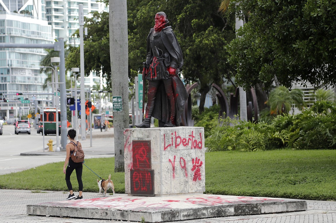 A woman walks past a vandalized statue of Juan Ponce de León at Bayfront Park in Miami, Thursday, June 11, 2020. Miami police say that several people were arrested for vandalizing the statue of Juan Ponce de León and Christopher Columbus during a protest Wednesday. Protests continue over the death of George Floyd, a black man who died last month while in police custody in Minneapolis. (AP Photo/Lynne Sladky)