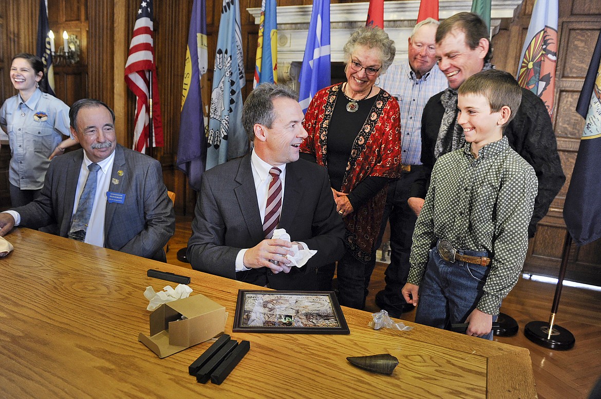 FILE - In this April 16, 2016, file photo, Montana Gov. Steve Bullock accepts a fossilized rib and tail vertebrae from a triceratops from Luke Phipps, 12, at the State Capitol in Helena, Mont., after the governor signed a bill to clarify that fossils are part of a property's surface rights, not its mineral rights, unless a contract separating the ownership says otherwise. The 9th U.S. Circuit Court of Appeals on June 17, 2020, upheld a federal judge's ruling that said dinosaur fossils are part of a property's surface estate in an ongoing battle over ownership of millions of dollars of fossils unearthed on an eastern Montana ranch. (Thom Bridge/Independent Record via AP, File)