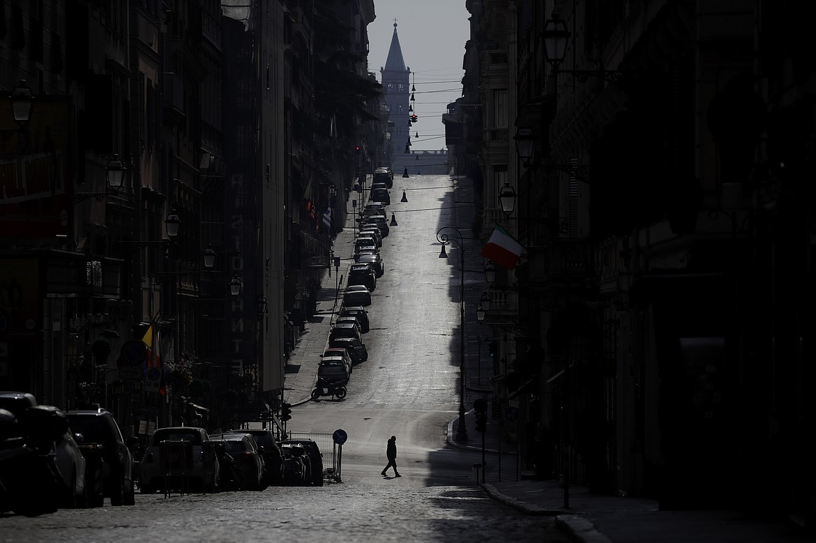 A man walks along a road leading to St. Mary Major Basilica, silhouetted in background, in Rome, Sunday, March 22, 2020. Italian Premier Giuseppe Conte has told the nation he is tightening the lockdown to fight the rampaging spread of coronavirus, shuttind down all production facilities except those that are "necessary, crucial, indispensible to guarantee" the good of the country. For most people, the new coronavirus causes only mild or moderate symptoms. For some it can cause more severe illness, especially in older adults and people with existing health problems. (AP Photo/Alessandra Tarantino)