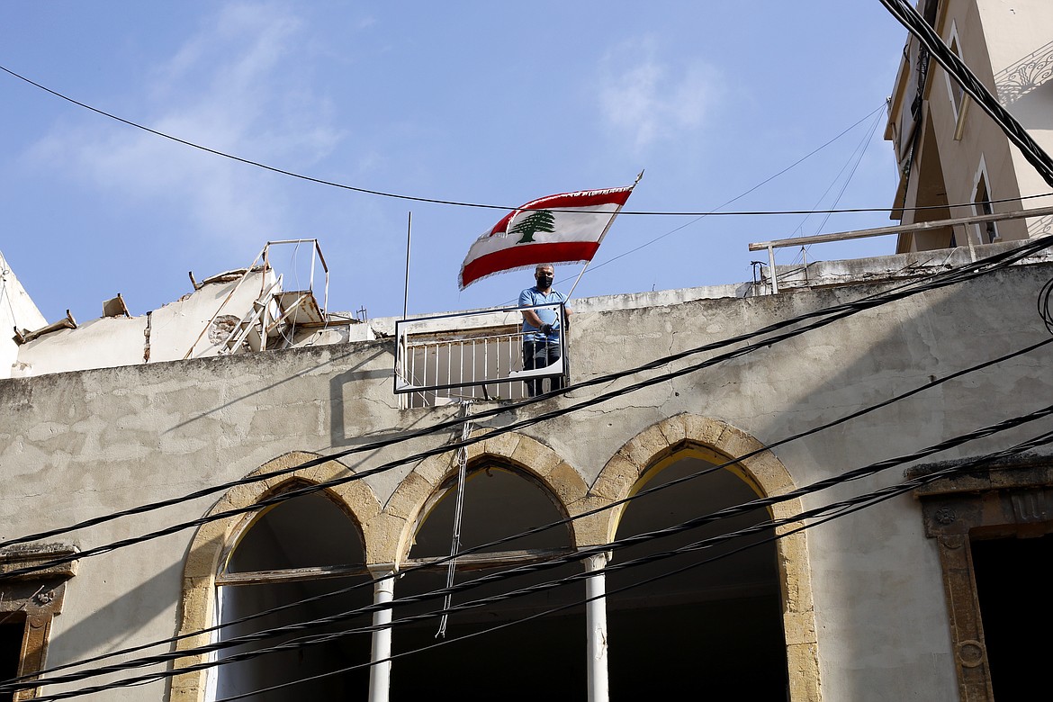A man puts a Lebanese flag on a roof of a damaged building at a neighborhood near the scene of Tuesday's explosion that hit the seaport of Beirut, Lebanon, Friday, Aug. 7, 2020. Rescue teams were still searching the rubble of Beirut's port for bodies on Friday, nearly three days after a massive explosion sent a wave of destruction through Lebanon's capital. (AP Photo/Thibault Camus)
