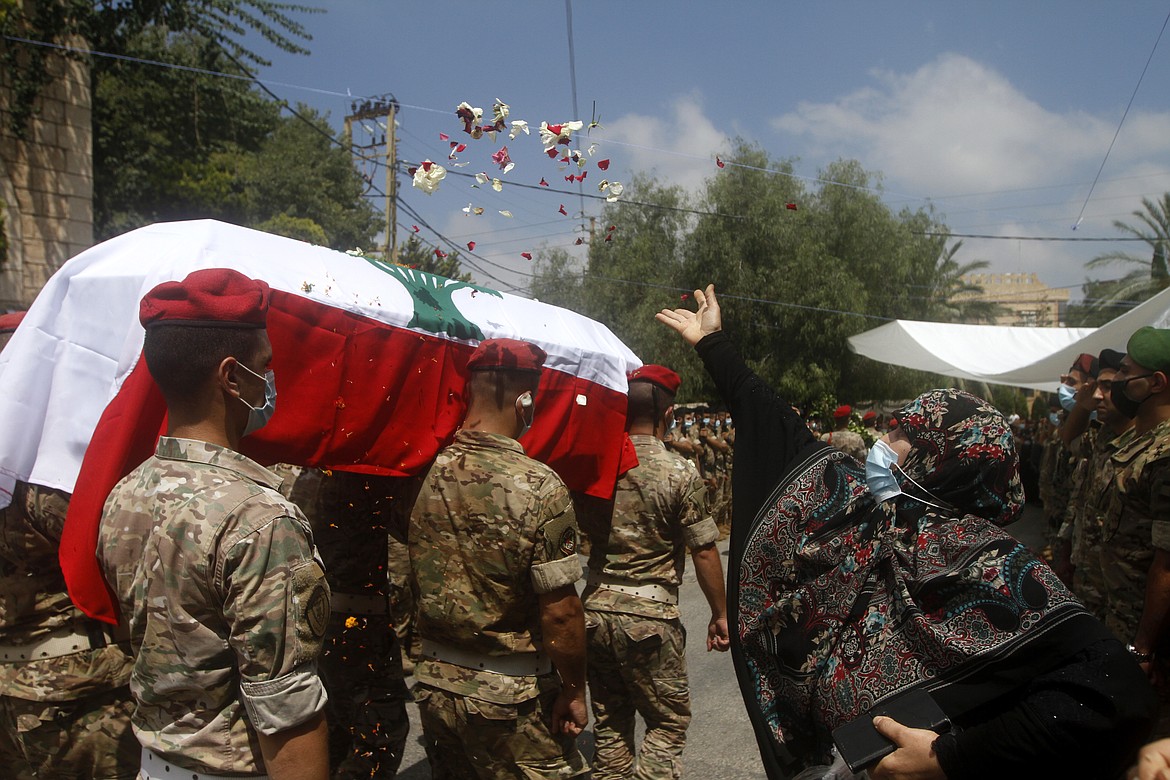 A woman throws flowers over Lebanese army soldiers who carry the coffin of lieutenant Ayman Noureddine, who was killed by Tuesday's explosion that hit the seaport of Beirut, during his funeral procession, in Numeiriyeh village, south Lebanon, Friday, Aug. 7, 2020. Rescue teams were still searching the rubble of Beirut's port for bodies on Friday, nearly three days after a massive explosion sent a wave of destruction through Lebanon's capital.  (AP Photo/Mohammed Zaatari)