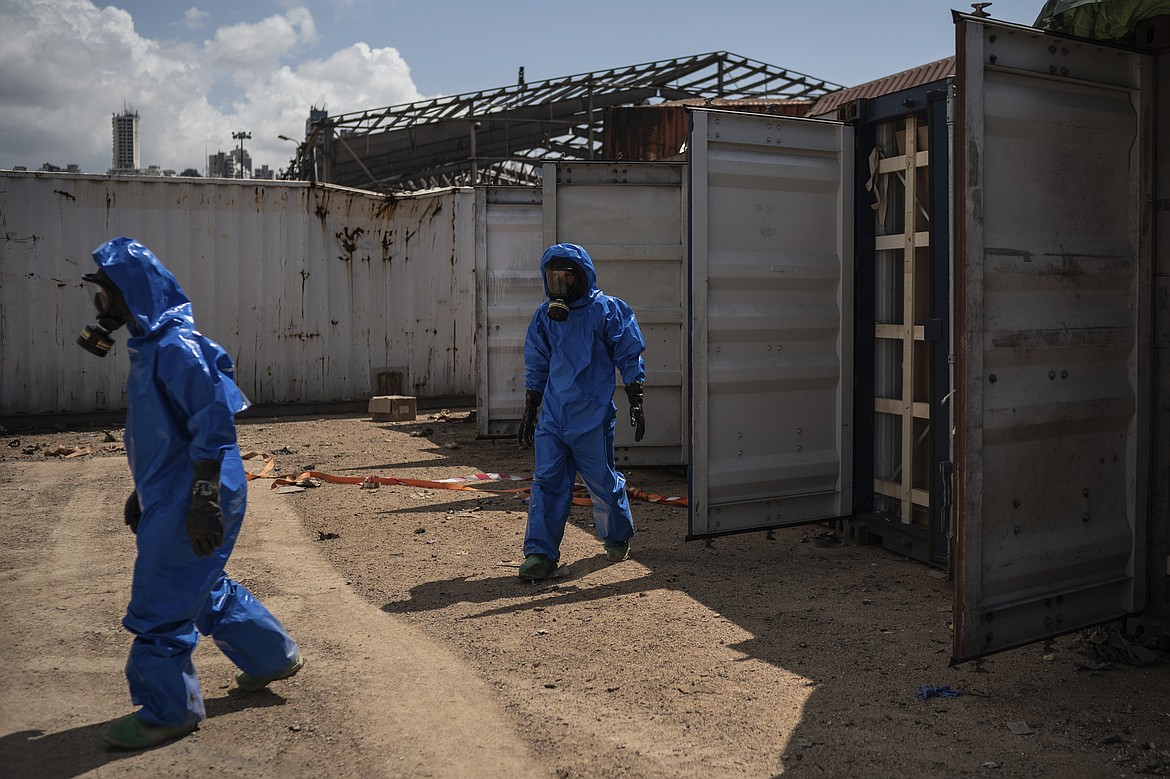 FILE - In this Aug. 10, 2020 file photo, French emergency workers, part of a special unit working with chemicals, walk next to damaged containers near the site of last week's explosion, in the port of Beirut, Lebanon. Lebanon's judicial investigation of the Beirut port explosion started with political wrangling over the naming of a lead investigator, military threats to jail leakers and doubts over whether a panel appointed along sectarian lines could be fully impartial. (AP Photo/Felipe Dana, File)