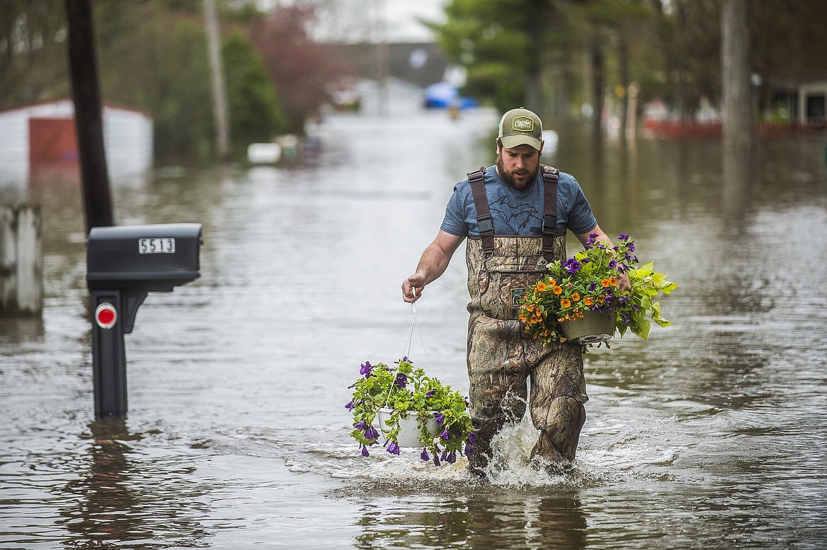 Tyler Marciniak, of Grand Rapids, carries hanging plants through floodwaters as he helps his father, Tom Marciniak, assess the damage to his home on Red Oak Drive on Wixom Lake, Tuesday, May 19, 2020, in Beaverton, Mich. (Katy Kildee/Midland Daily News via AP)
