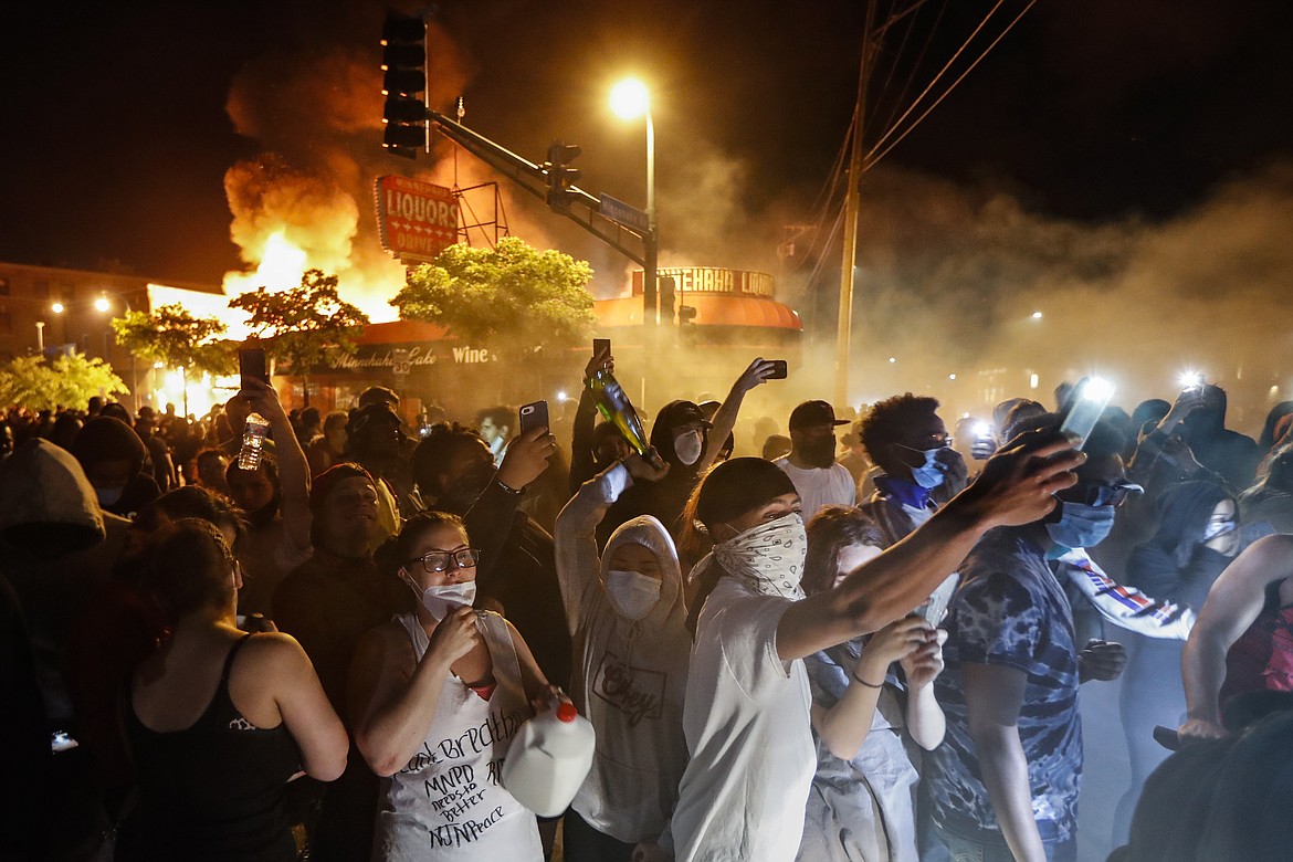 Protestors demonstrate outside of a burning liquor store near the Minneapolis 3rd Police Precinct, Thursday, May 28, 2020, in Minneapolis. Protests over the death of George Floyd, a black man who died in police custody Monday, broke out in Minneapolis for a third straight night. (AP Photo/John Minchillo)