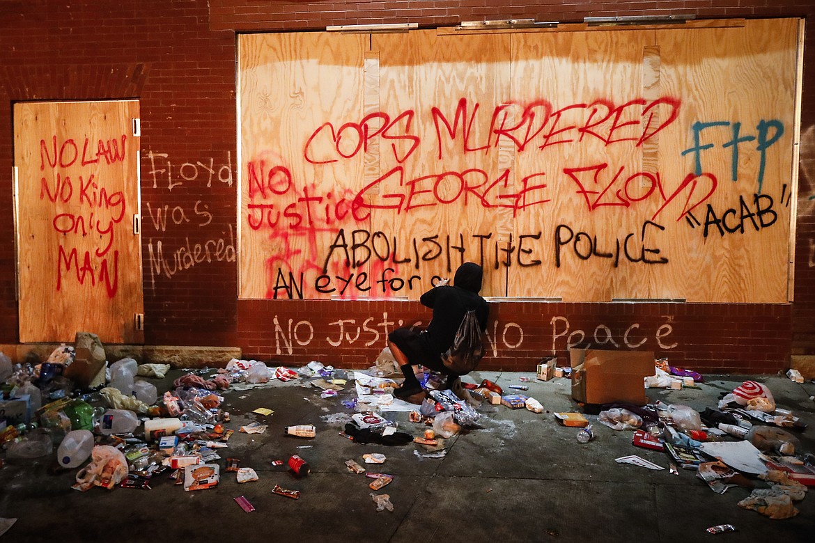 A protestor sprays graffiti on a wall near the Minneapolis 3rd Police Precinct, Thursday, May 28, 2020, in Minneapolis. Protests over the death of George Floyd, a black man who died in police custody Monday, broke out in Minneapolis for a third straight night. (AP Photo/John Minchillo)