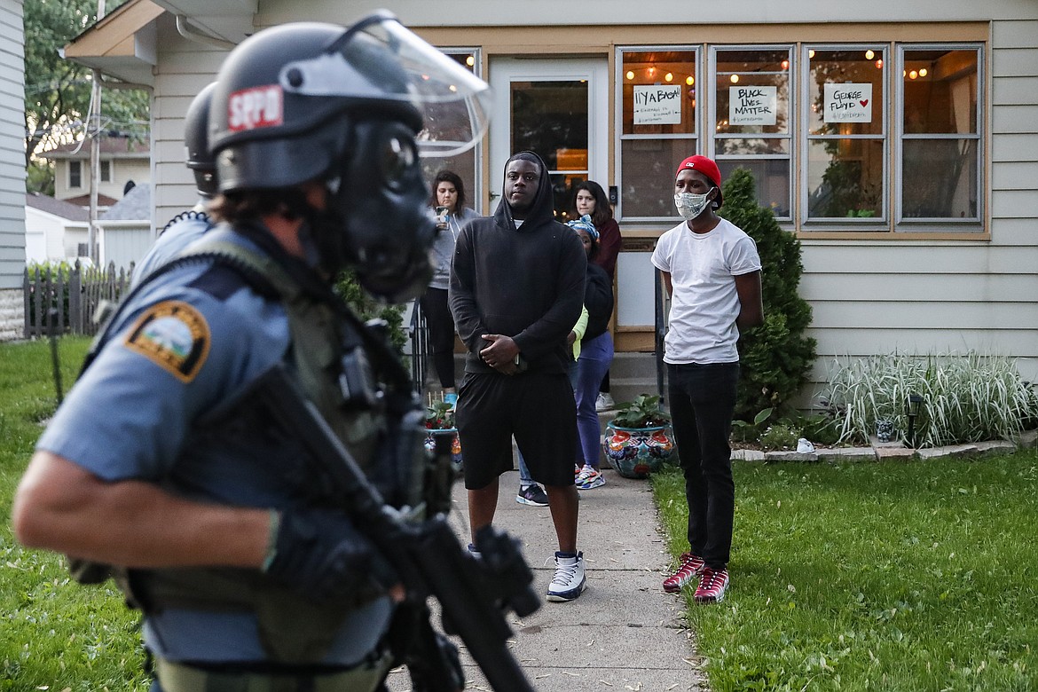 Protestors watch as police in riot gear walk down a residential street, Thursday, May 28, 2020, in St. Paul, Minn. Protests over the death of George Floyd, a black man who died in police custody Monday, broke out in Minneapolis for a third straight night. (AP Photo/John Minchillo)