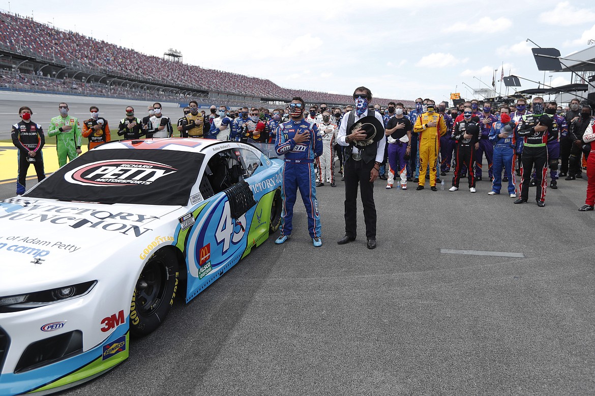 Driver Bubba Wallace, front left, and team owner Richard Petty, front right, stand for the National Anthem in the pits of the Talladega Superspeedway prior to the start of the NASCAR Cup Series auto race at the Talladega Superspeedway in Talladega Ala., Monday June 22, 2020. In an extraordinary act of solidarity with NASCAR’s only Black driver, dozens of drivers pushed the car belonging to Bubba Wallace to the front of the field before Monday’s race as FBI agents nearby tried to find out who left a noose in his garage stall over the weekend. (AP Photo/John Bazemore)