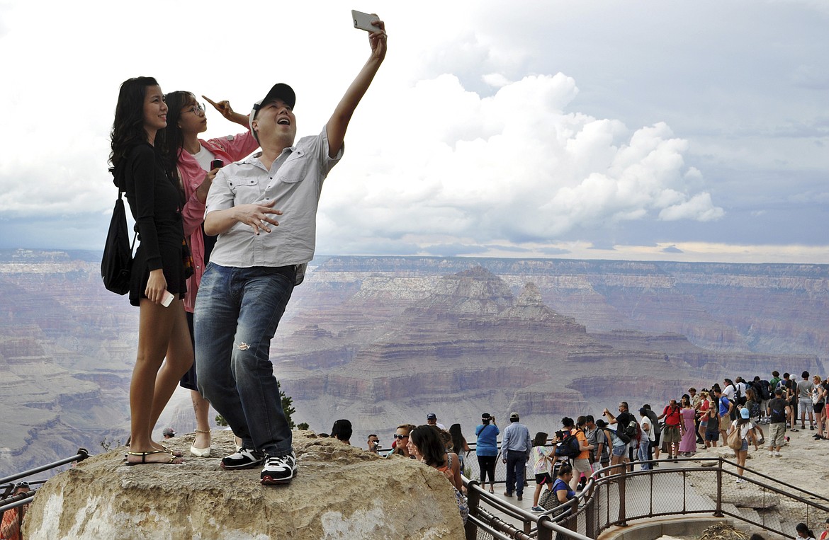 FILE - In this Aug. 2, 2015, file photo, tourists Joseph Lin, Ning Chao, center, and Linda Wang, left, pose for a selfie along the south rim at Grand Canyon National Park, Ariz. Parks around the country are grappling with how best to expand service while preserving the pristine nature. One of the latest debates is playing out at the Grand Canyon where park officials are road mapping future telecommunications towers. The handful that exist now are prominent among the park lodging, visitor center and residential area. (Emery Cowan/Arizona Daily Sun via AP, File)