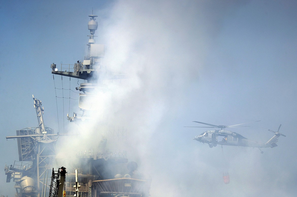 A helicopter approaches the USS Bonhomme Richard as crews fight the fire, Monday, July 13, 2020, in San Diego. Fire crews continue to battle the blaze Monday after numerous people suffered minor injuries in an explosion and fire Sunday on board the USS Bonhomme Richard at Naval Base San Diego. (AP Photo/Gregory Bull)