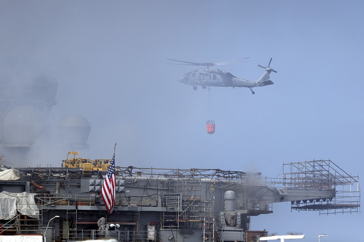 A helicopter approaches the USS Bonhomme Richard as crews fight the fire, Monday, July 13, 2020, in San Diego. Fire crews continue to battle the blaze Monday after 21 people suffered minor injuries in an explosion and fire Sunday on board the USS Bonhomme Richard at Naval Base San Diego. (AP Photo/Gregory Bull)