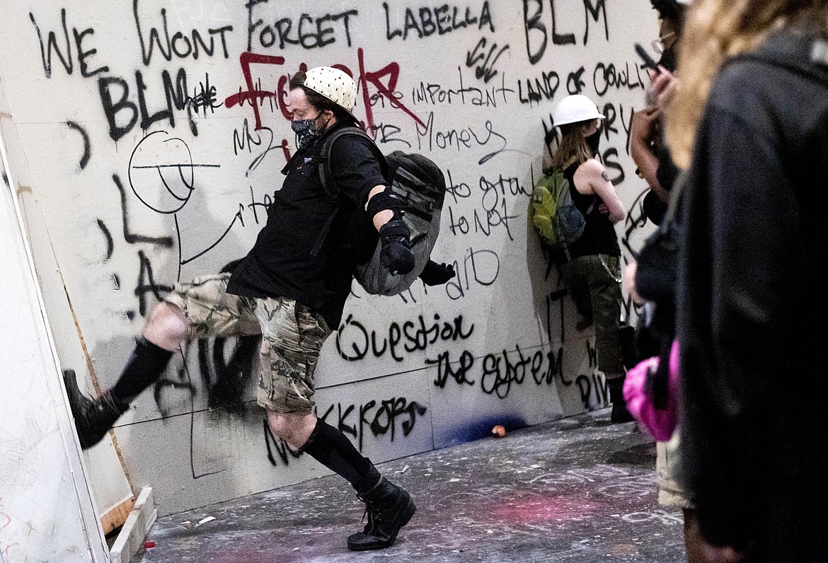 A protester kicks in temporary boarding at the Mark O. Hatfield United States Courthouse in Portland, Ore. on July 19, 2020, Federal officers emerged from the building and used teargas and crowd control munitions to disperse the crowd. (AP Photo/Noah Berger)