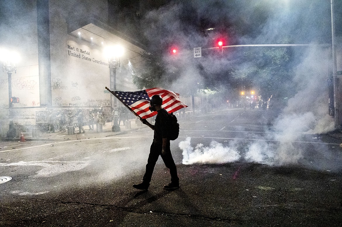 A Black Lives Matter protester carries an American flag as teargas fills the air outside the Mark O. Hatfield United States Courthouse in Portland, Ore. on July 21, 2020. (AP Photo/Noah Berger)