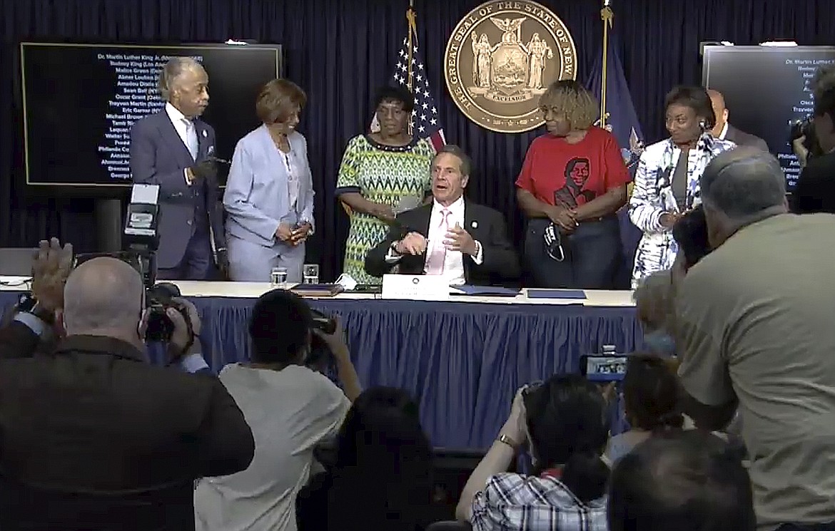 In this photo made from video provided by the office of New York Governor Andrew M. Cuomo, Gov. Cuomo, center, reacts after signing into law, Friday, June 12, 2020, in New York, a sweeping package of police accountability measures that received new backing following protests of George Floyd's killing. The laws signed by Cuomo, a Democrat, will ban police chokeholds, make it easier to sue people who call police on others without good reason, and set up a special prosecutor's office to investigate the deaths of people during and following encounters with police officers. (Office of New York Governor Andrew M. Cuomo via AP)