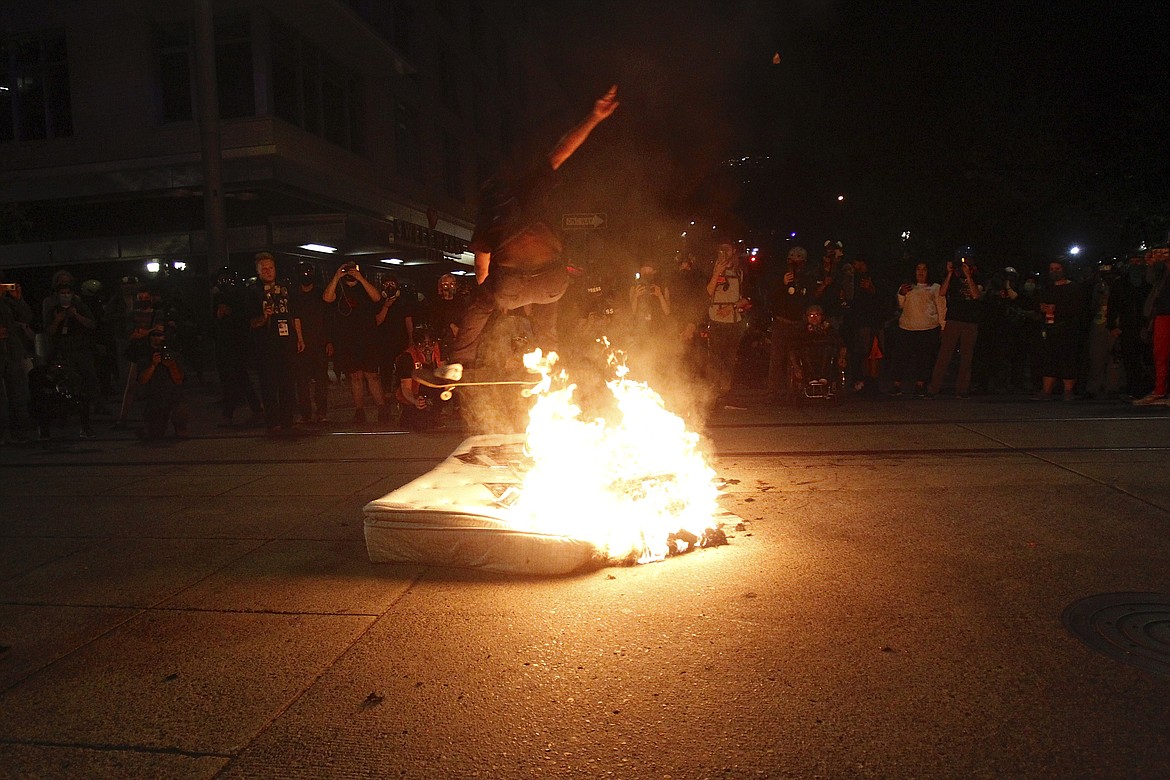 A protester jumps over a fire on his skateboard on Wednesday, Aug. 19, 2020. Protesters in Portland have clashed with federal agents for the first time since July in a demonstration that targeted a U.S. Immigration and Customs Enforcement building.(Sean Meagher/The Oregonian via AP)