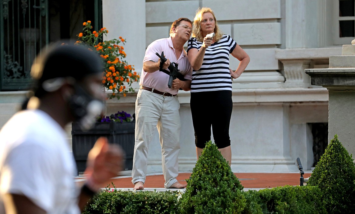 FILE - In this June 28, 2020 file photo, armed homeowners Mark and Patricia McCloskey, standing in front their house along Portland Place confront protesters marching to St. Louis Mayor Lyda Krewson's house in the Central West End of St. Louis. St. Louis’ top prosecutor told The Associated Press on Monday, July 20, 2020 that she is charging a white husband and wife with felony unlawful use of a weapon for displaying guns during a racial injustice protest outside their mansion. (Laurie Skrivan/St. Louis Post-Dispatch via AP File)