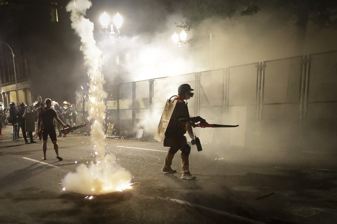 Demonstrators walk along a steel fence as federal officers launch tear gas during a Black Lives Matter protest at the Mark O. Hatfield United States Courthouse Sunday, July 26, 2020, in Portland, Ore. (AP Photo/Marcio Jose Sanchez)