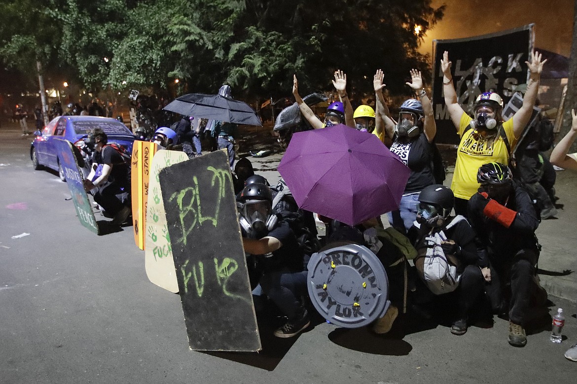 EDS NOTE: OBSCENITY - Demonstrators, including members of the "Wall of Moms," top right, shield themselves from crowd control munitions and tear gas launched by federal officers during a Black Lives Matter protest at the Mark O. Hatfield United States Courthouse Wednesday, July 29, 2020, in Portland, Ore. (AP Photo/Marcio Jose Sanchez)