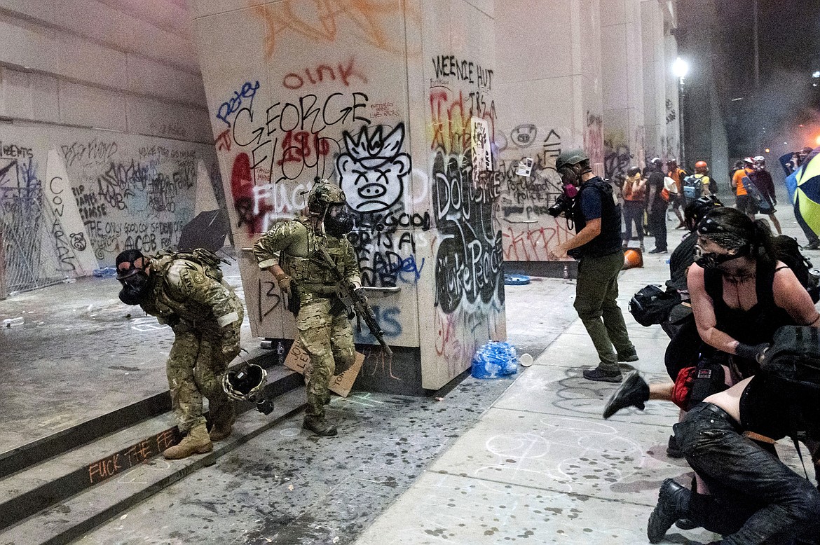 EDS NOTE: OBSCENITY - Federal officers disperse protesters at the Mark O. Hatfield United States Courthouse on Tuesday, July 21, 2020, in Portland, Ore.  Federal officers’ actions at protests in Oregon’s largest city, hailed by President Donald Trump but done without local consent, are raising the prospect of a constitutional crisis — one that could escalate as weeks of demonstrations find renewed focus in clashes with camouflaged, unidentified agents outside Portland’s U.S. courthouse.(AP Photo/Noah Berger)