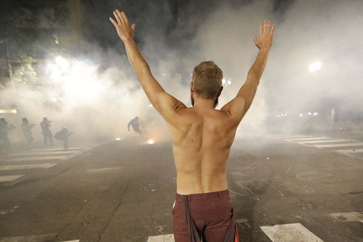 A demonstrator holds his arms up in the air as federal officers launch tear gas during a Black Lives Matter protest at the Mark O. Hatfield United States Courthouse Tuesday, July 28, 2020, in Portland, Ore. (AP Photo/Marcio Jose Sanchez)