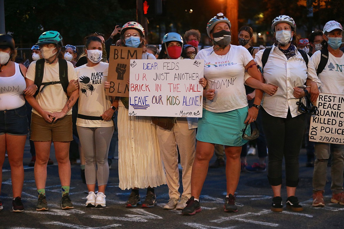 A group of mothers stand arm-in-arm outside the federal building and Justice Center in downtown Portland, Ore., on Saturday, July 18, 2020, during another night of protests in Portland. (Mark Graves/The Oregonian via AP)