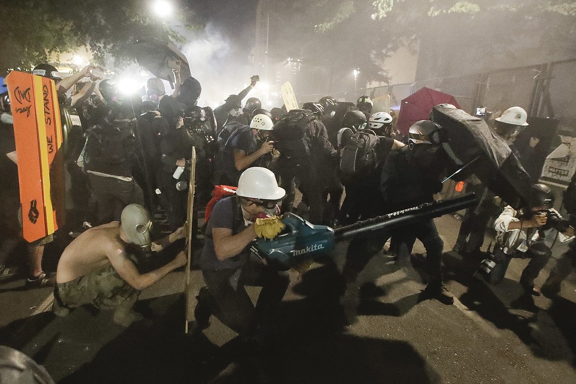 Demonstrators huddle and blow back tear gas with leaf blowers during clashes with federal officers during a Black Lives Matter protest at the Mark O. Hatfield United States Courthouse Wednesday, July 29, 2020, in Portland, Ore. (AP Photo/Marcio Jose Sanchez)