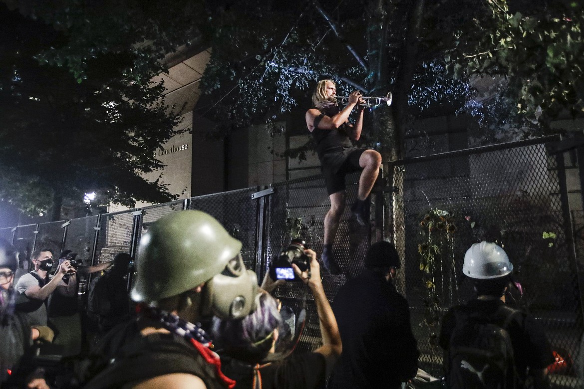 A demonstrator plays a trumpet from atop a steel fence during a Black Lives Matter protest at the Mark O. Hatfield United States Courthouse Sunday, July 26, 2020, in Portland, Ore. (AP Photo/Marcio Jose Sanchez)