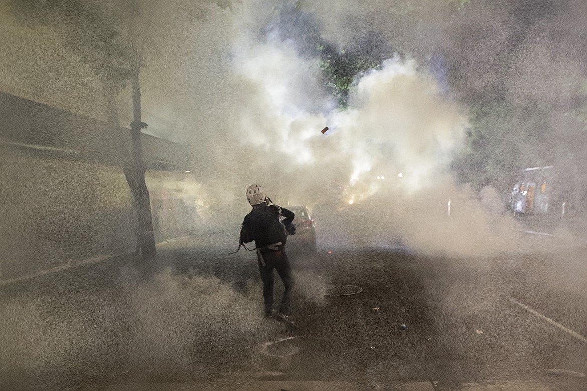 A demonstrator throws a tear gas canister back at federal officers during a Black Lives Matter protest at the Mark O. Hatfield United States Courthouse Tuesday, July 28, 2020, in Portland, Ore. (AP Photo/Marcio Jose Sanchez)