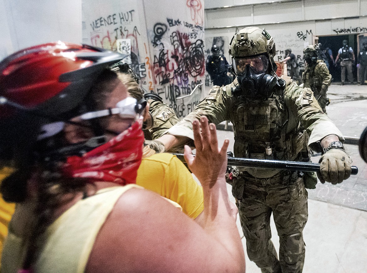 A federal officer pushes back demonstrators at the Mark O. Hatfield United States Courthouse on Tuesday, July 21, 2020, in Portland, Ore.  A federal judge is hearing arguments on Oregon's request for a restraining order against federal agents who have been sent to the state's largest city to quell protests that have spiraled into nightly clashes between authorities and demonstrators.(AP Photo/Noah Berger)