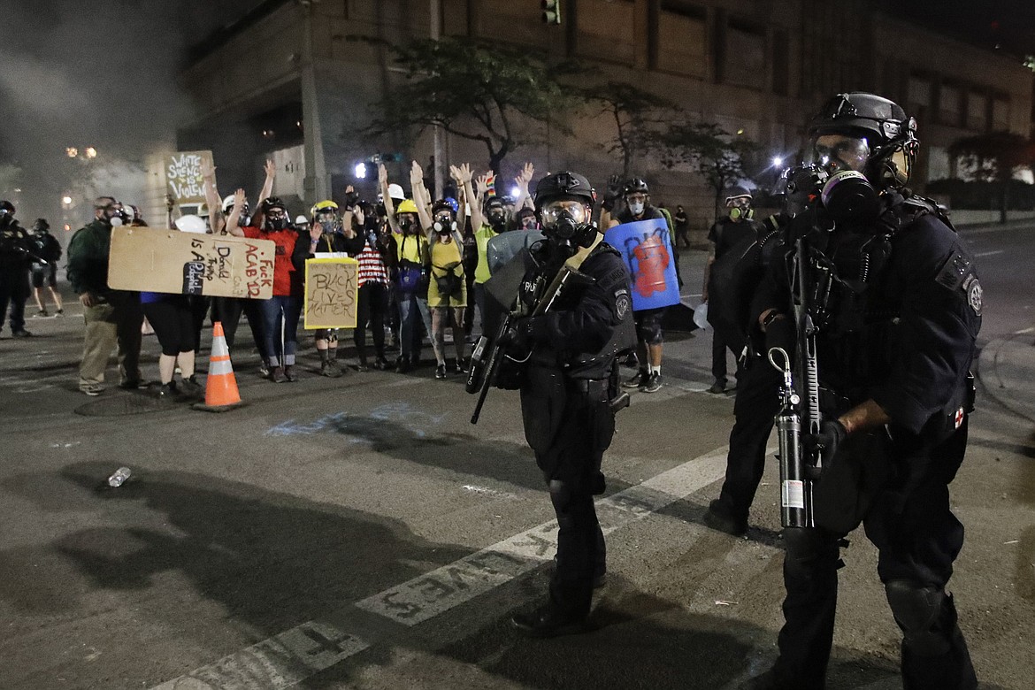 Demonstrators hold their arms up behind federal officers during a Black Lives Matter protest at the Mark O. Hatfield United States Courthouse Monday, July 27, 2020, in Portland, Ore. (AP Photo/Marcio Jose Sanchez)