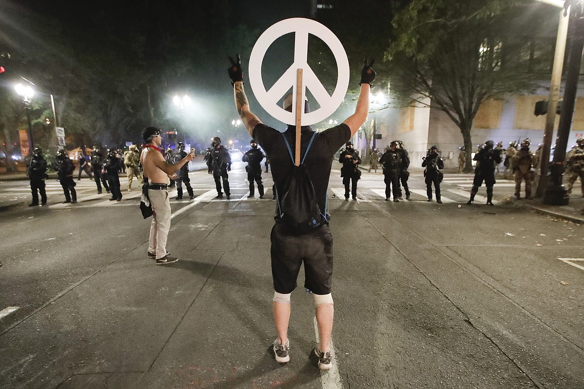 A demonstrator flashes a peace sign at federal officers during a Black Lives Matter protest at the Mark O. Hatfield United States Courthouse Wednesday, July 29, 2020, in Portland, Ore. (AP Photo/Marcio Jose Sanchez)