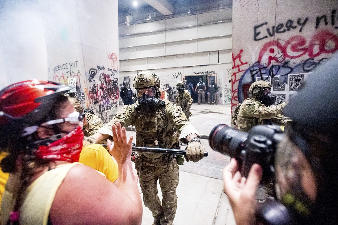 A federal officer pushes back demonstrators at the Mark O. Hatfield United States Courthouse on Tuesday, July 21, 2020, in Portland, Ore.  A federal judge is hearing arguments on Oregon's request for a restraining order against federal agents who have been sent to the state's largest city to quell protests that have spiraled into nightly clashes between authorities and demonstrators.(AP Photo/Noah Berger)